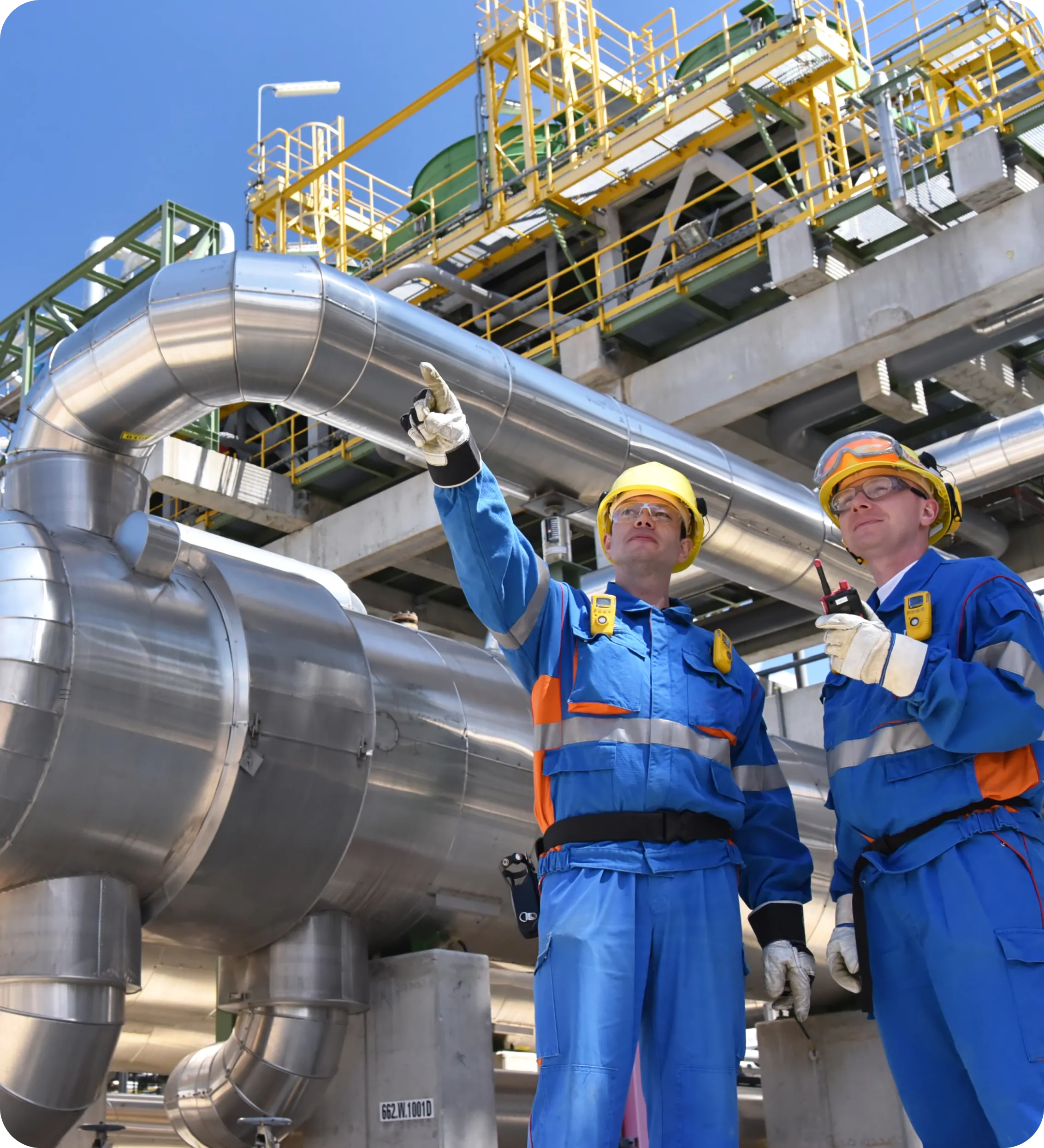 Two men in blue work clothes standing next to a pipe.